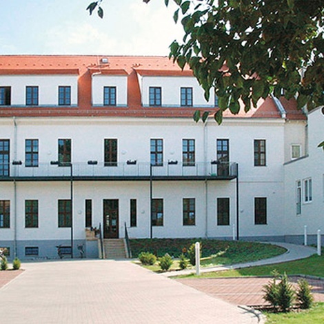 Standort Palais Bose, Rückansicht, ein Weg führt durch eine Grünanlage, Bäume sind mit Rindenmulch gedüngt, Terrasse und Balkone sichtbar